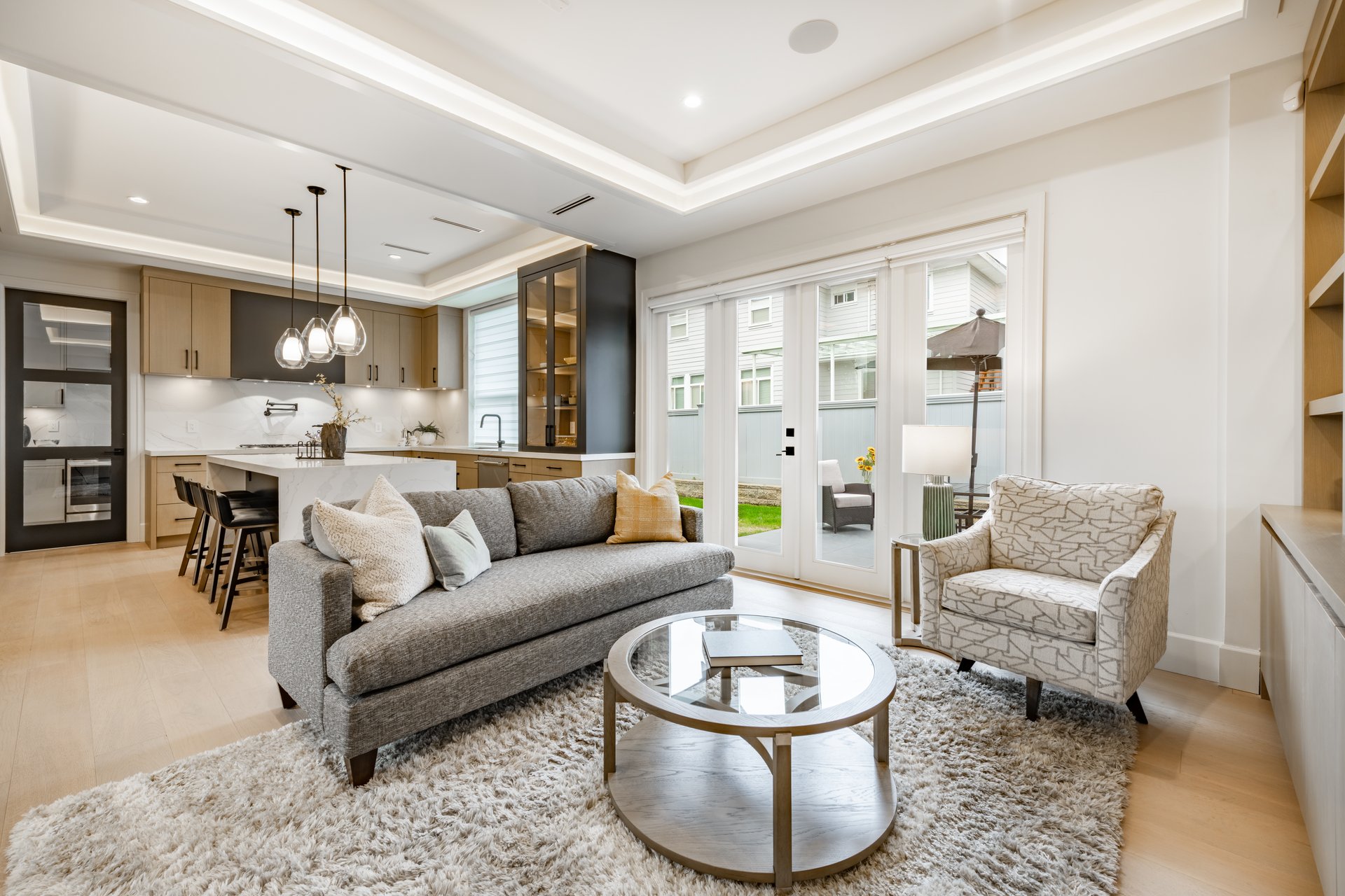 spacious living room in a newly constructed home staged professionally with fireplace view to kitchen grey sofa area rug built in cabinets and shelving recessed lighting in the ceiling modern new furniture
