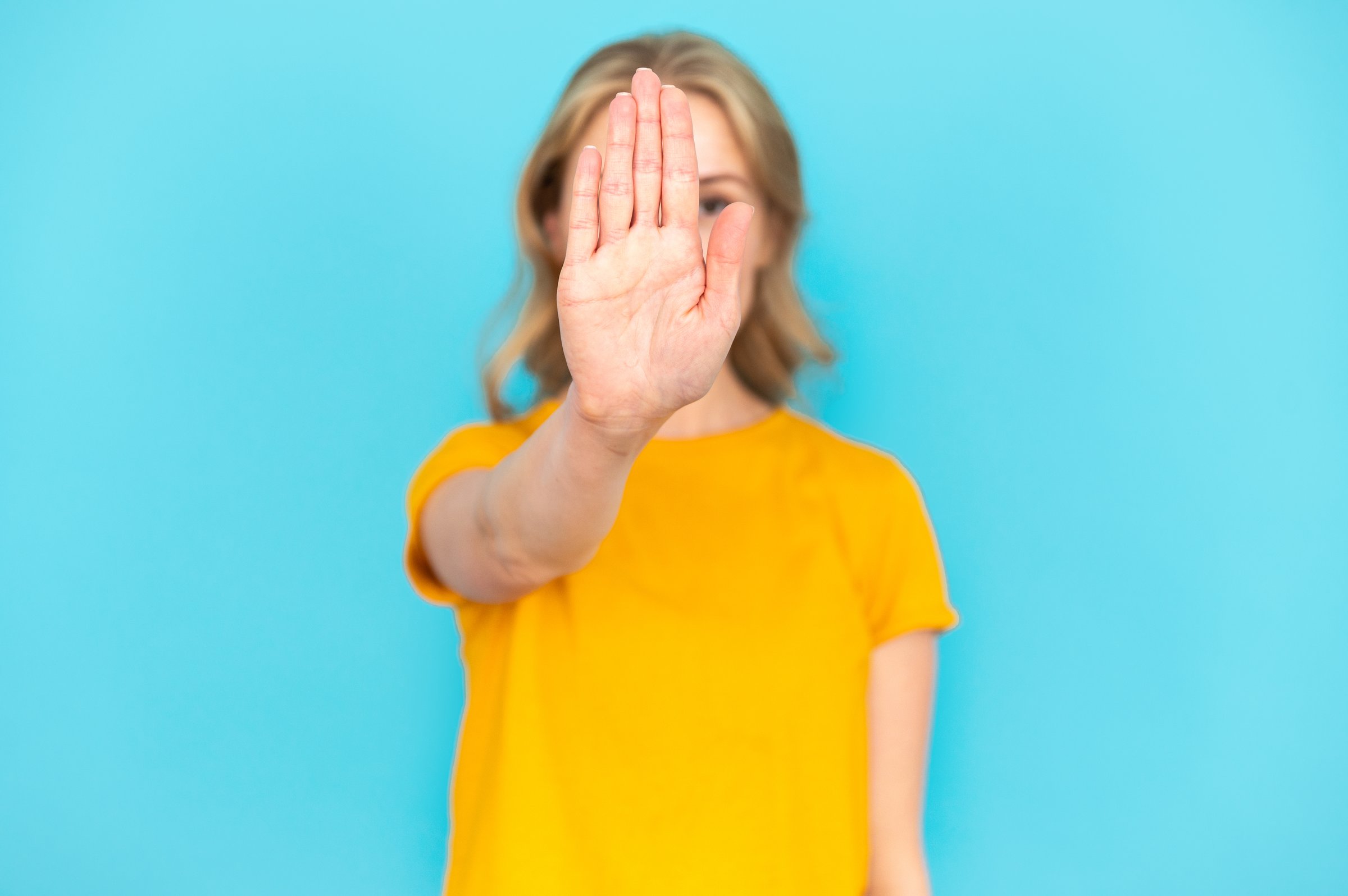 Selective focus on woman hand making stop sign against blurred studio background. Showing disagreement gesture. Saying no, denying, rejecting proposition, protesting against domestic violence, abuse.
