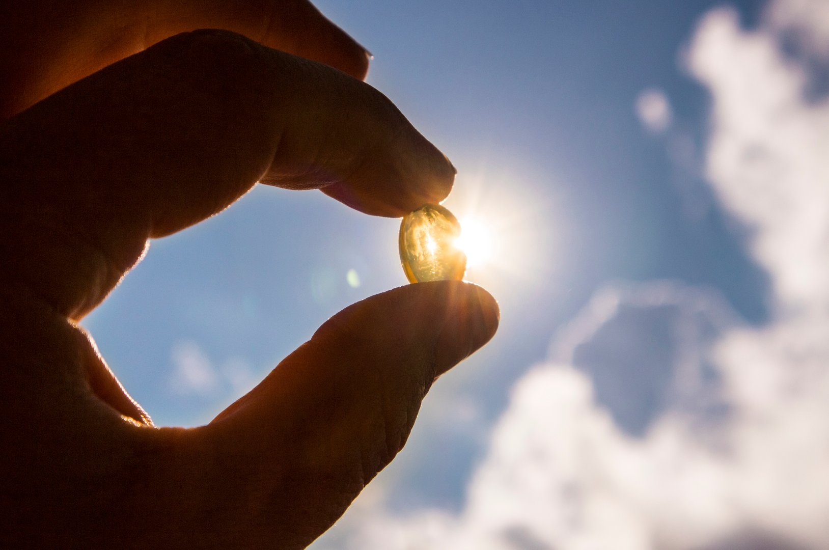 Vitamin D supplement capsule against sun and blue sky