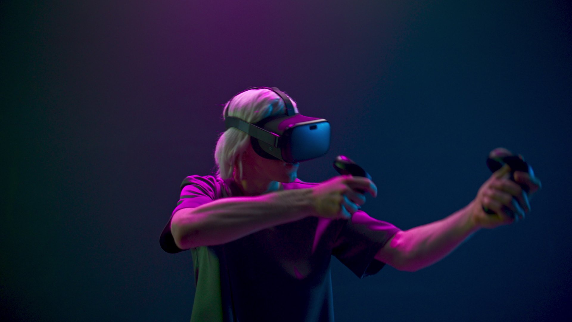 Emotional man playing shooter using joysticks closeup. VR glasses guy hands gesturing gun enjoying futuristic game neon light background. Gamer hitting target slow motion. Metaverse technology concept