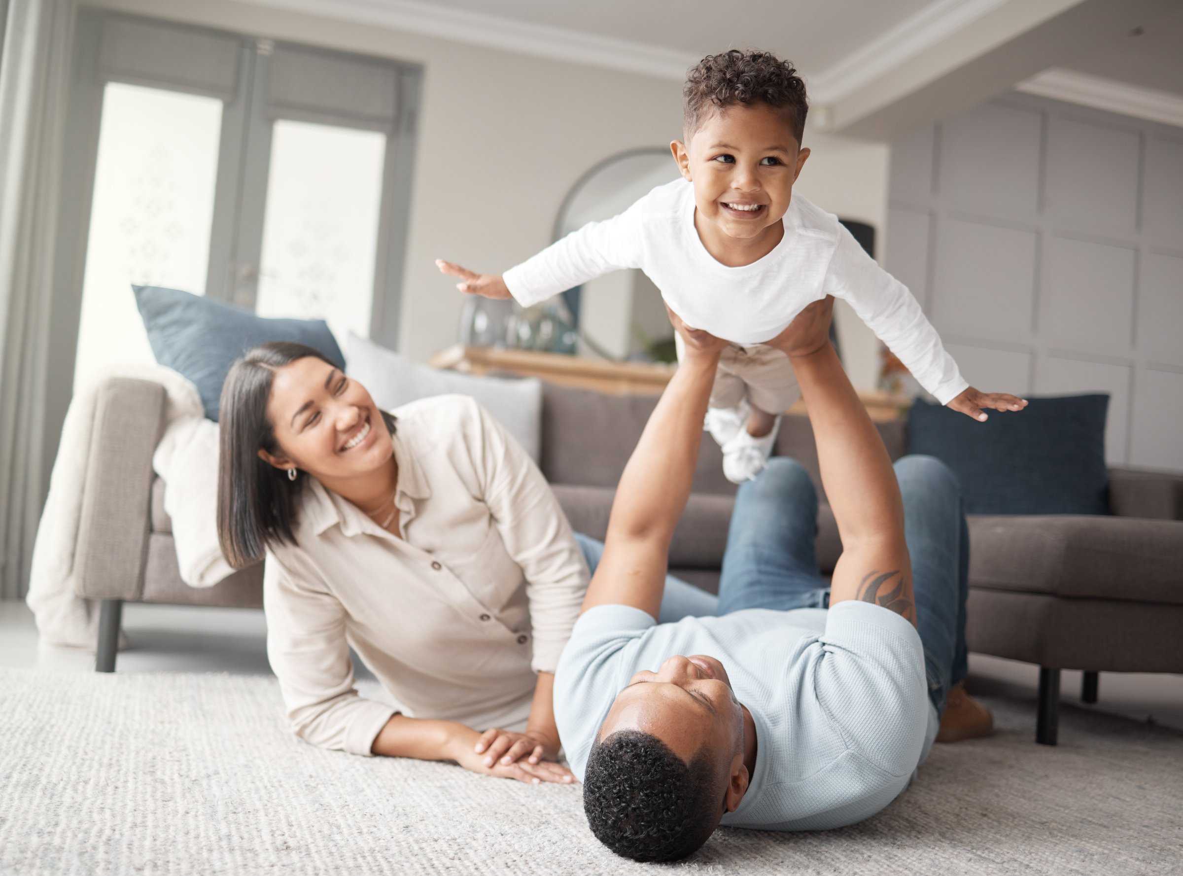 A happy mixed race family of three relaxing on the lounge floor and being playful together. Loving black family bonding with their son while playing fun games on the carpet at home