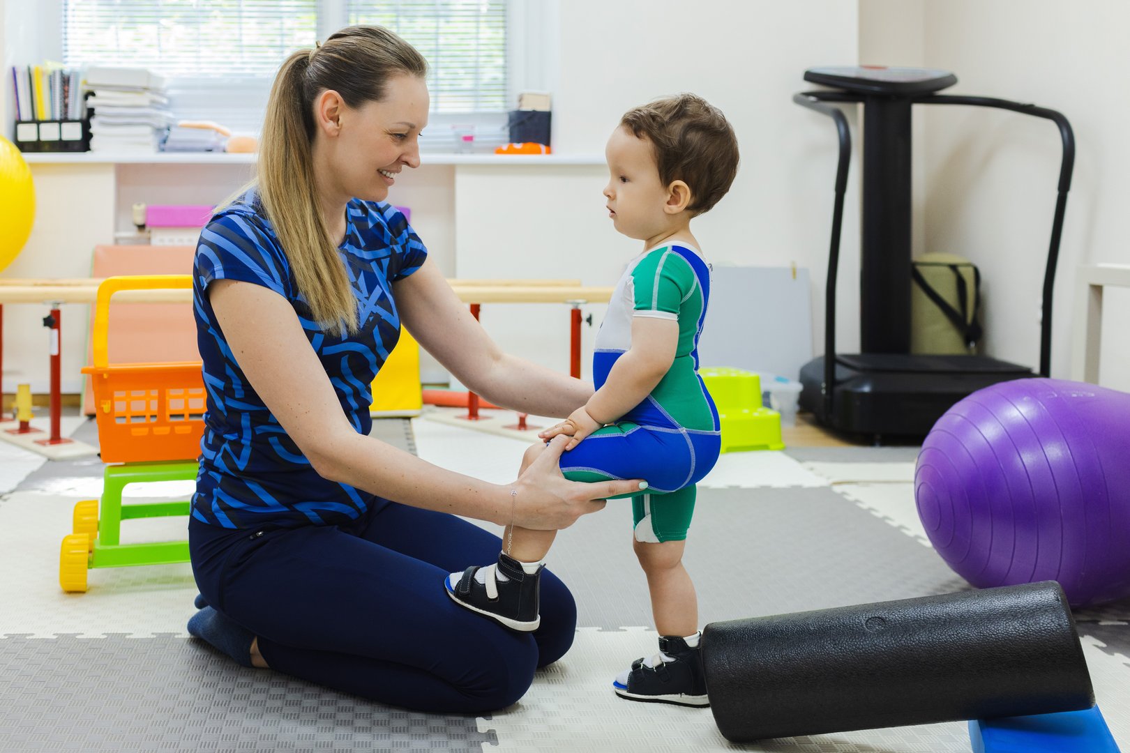 Physiotherapist assisting a little child with coordination disorders during motor skills development exercise in rehab clinic. Physiotherapy