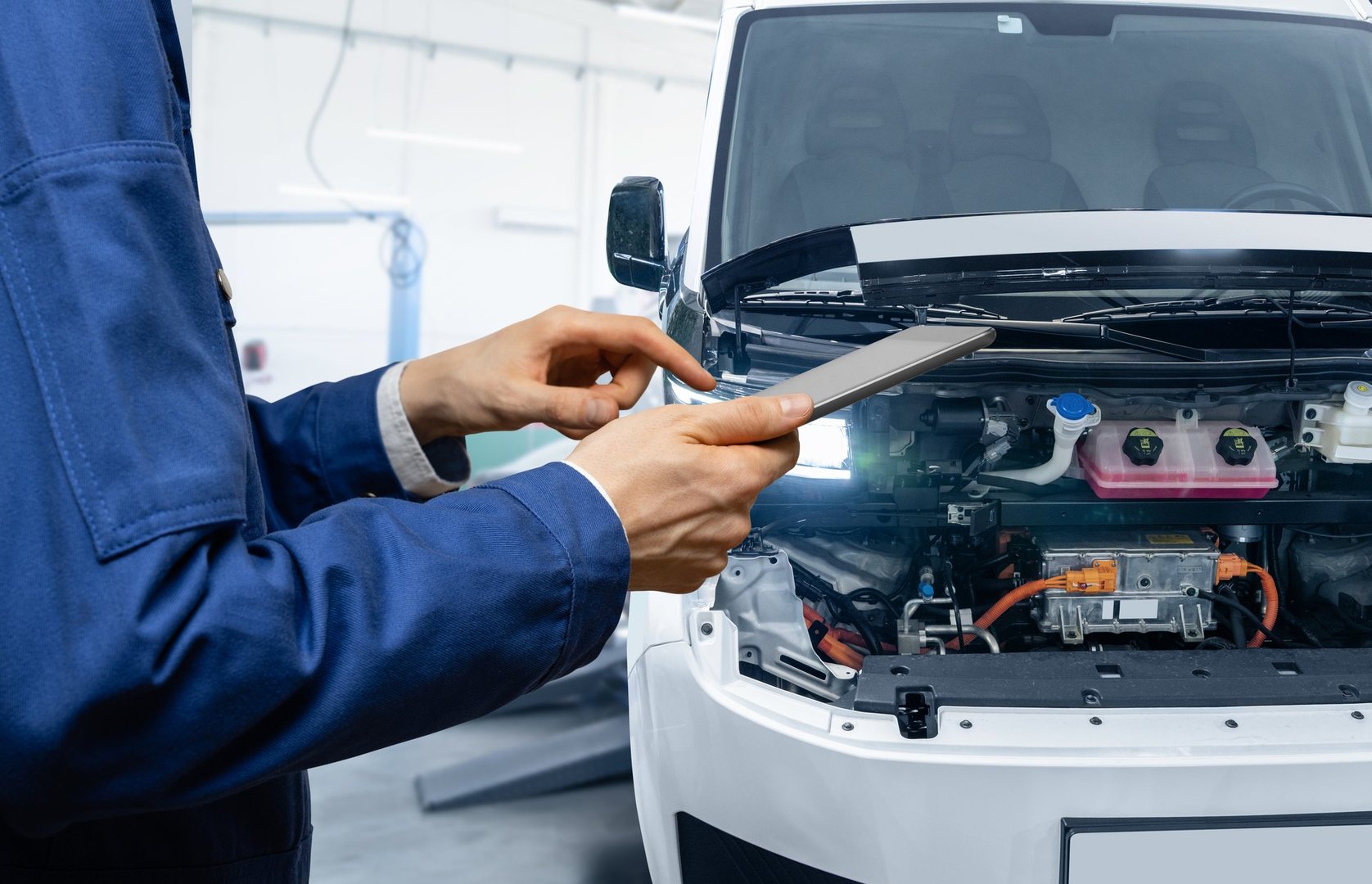 Serviceman with digital tablet next to electric van with open hood. Electric vehicles maintenance.