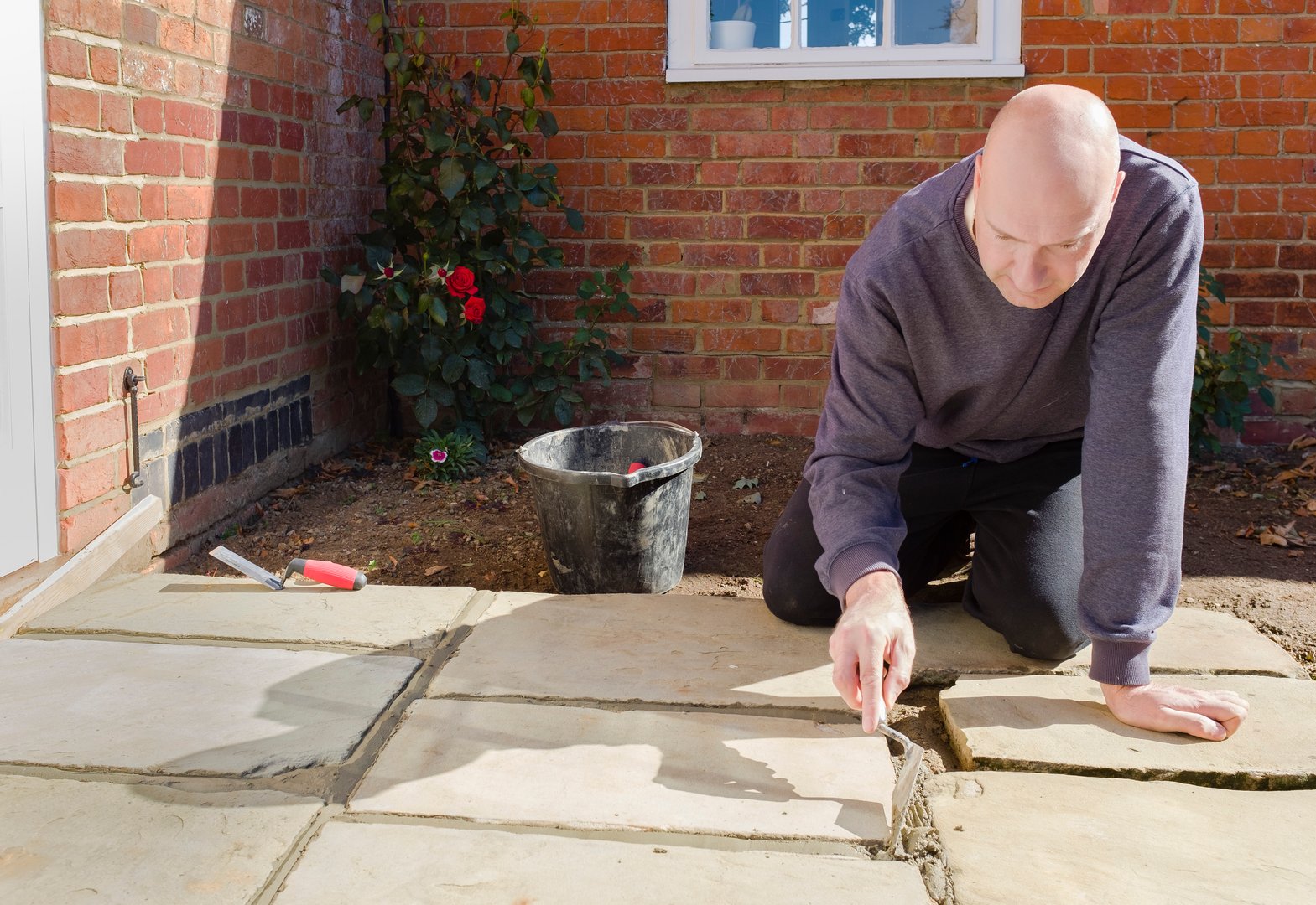 Builder laying and grouting York stone paving slabs outdoors, DIY home patio project , UK