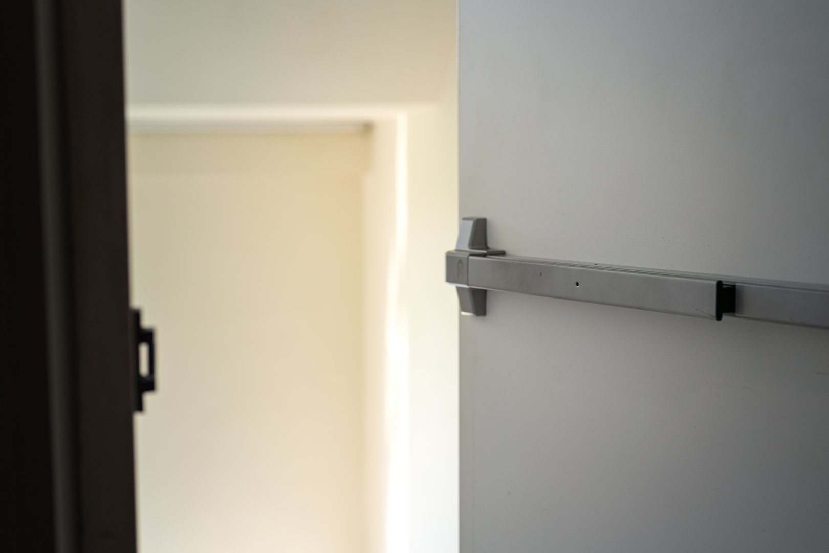 Fire exit metal door in opening position with background of the stairway with railing handle, using for emergency escape route. Building interior part photo, selective focus.