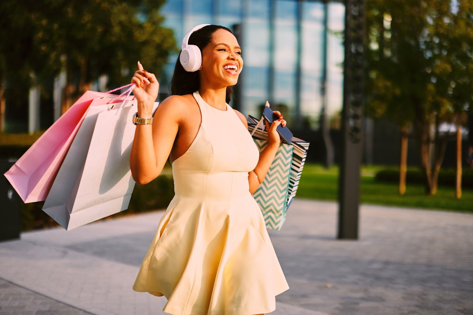 Joyful young woman walking outdoors carrying shopping bags and wearing headphones