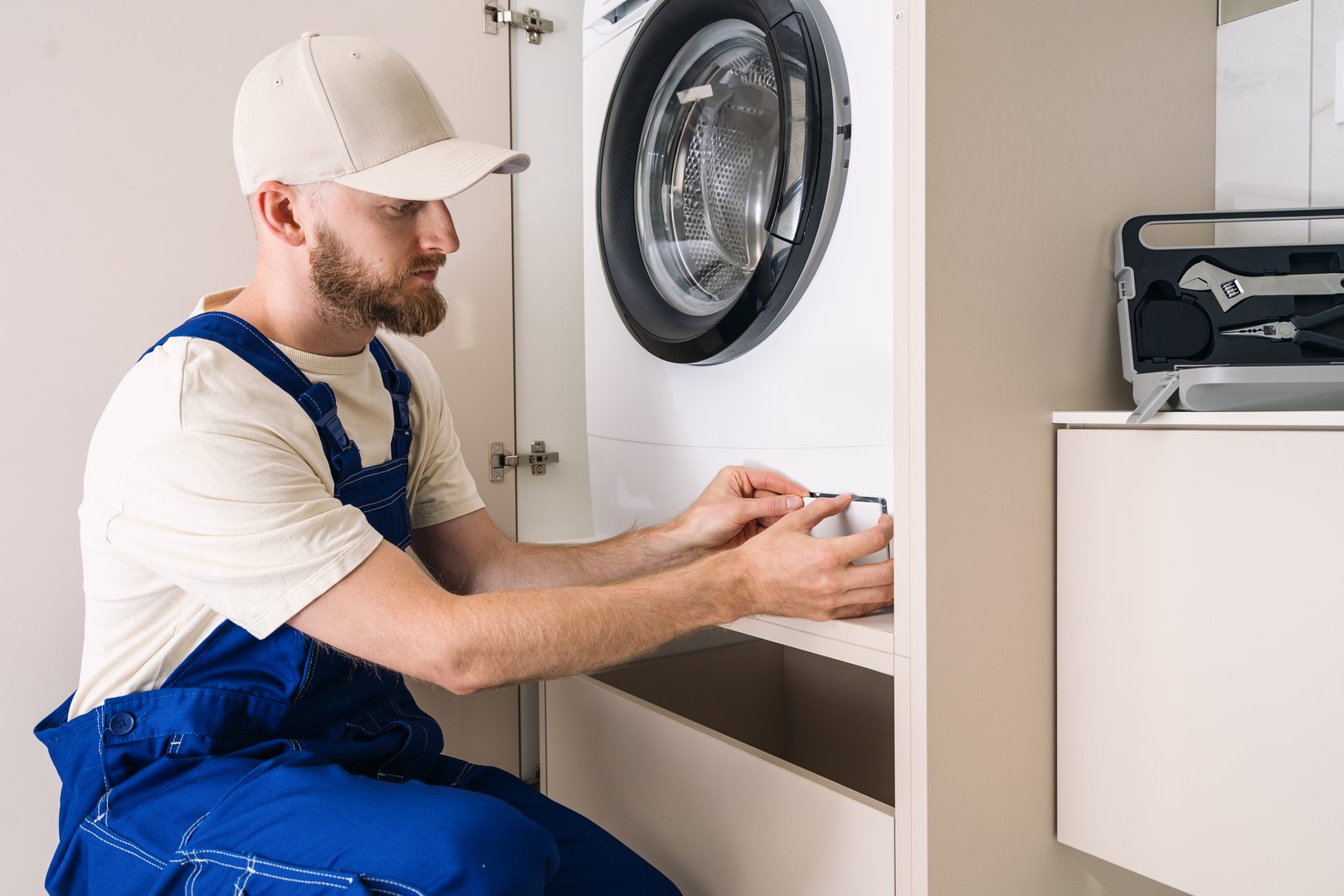 A skilled technician is checking clogged drain, open filter cover at automatic washing machine. Concepts of household appliances warranty service, repairing laundry room equipment