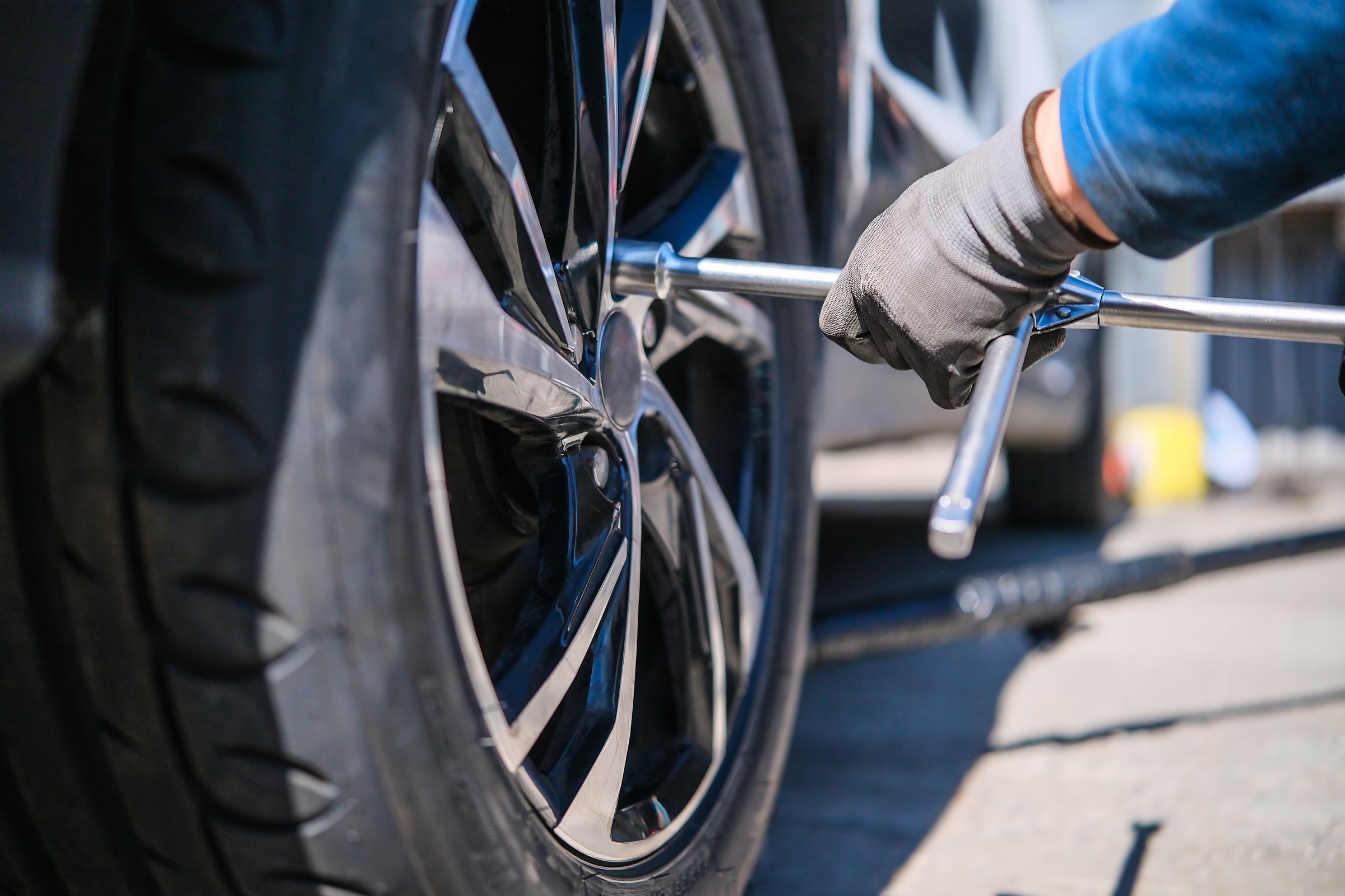 A tire mechanic unscrews the wheel bolts. Mechanic's hands use a wrench to change a wheel.