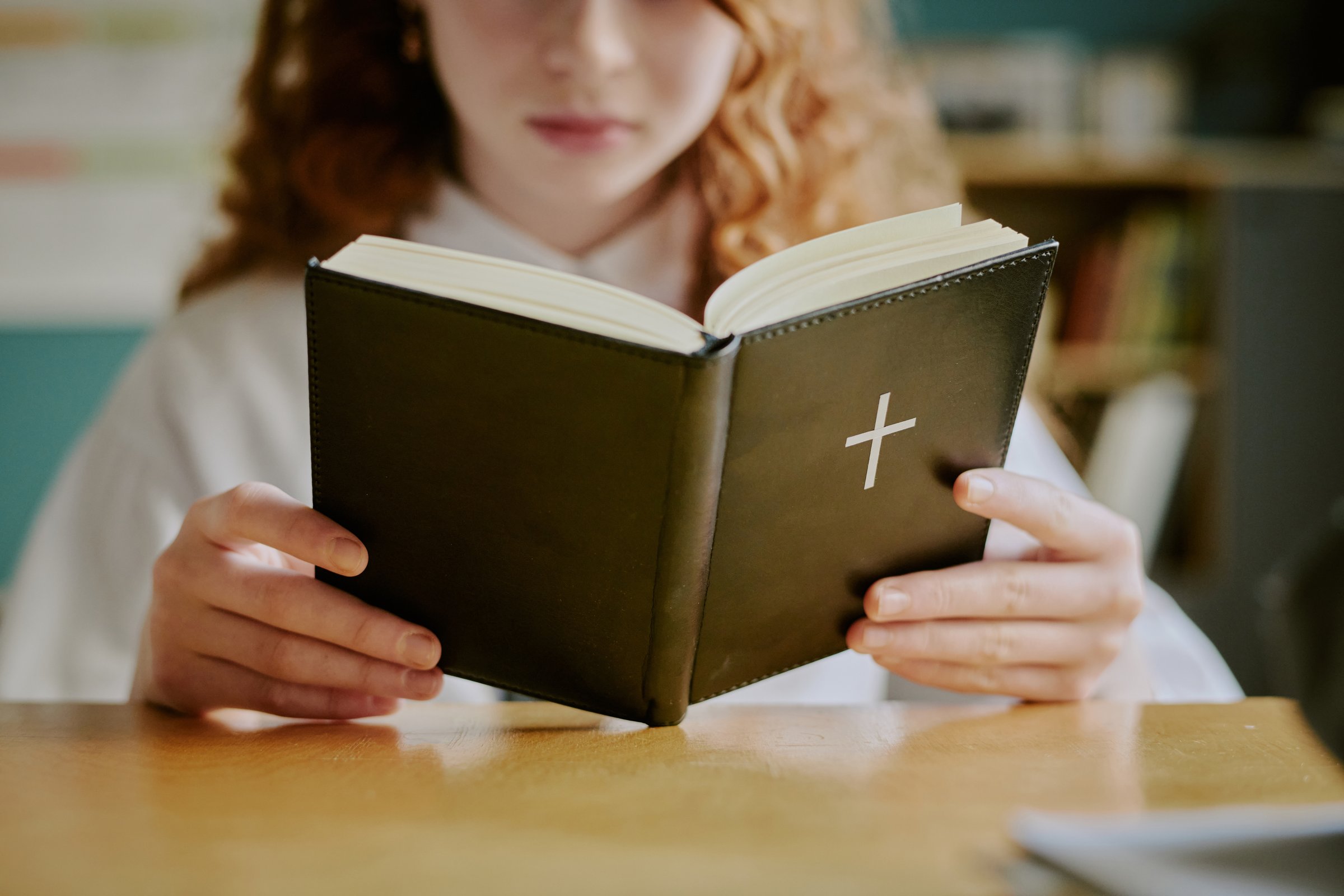 Schoolgirl reading religious book with reflective expression, focusing on text in quiet setting with soft background focus
