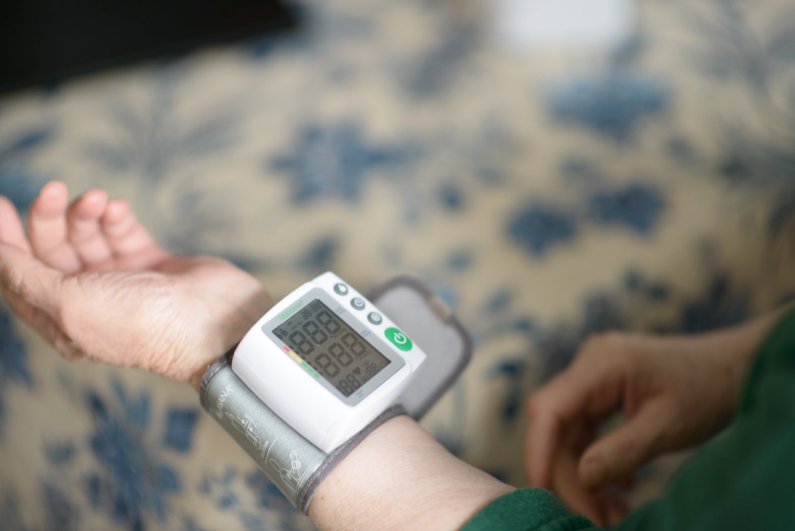 A senior woman measures her blood pressure with a home monitor