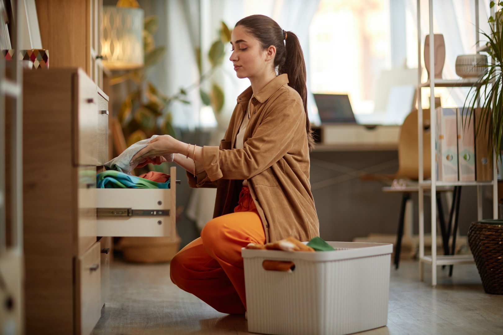Side view portrait of young woman storing clean clothes in drawers and enjoying laundry day, copy space