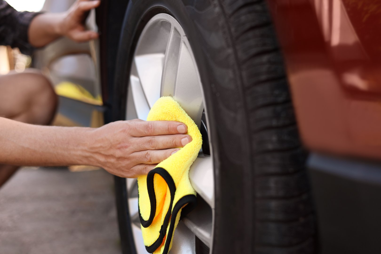 Man wiping car wheel with yellow microfiber rag outdoors, closeup