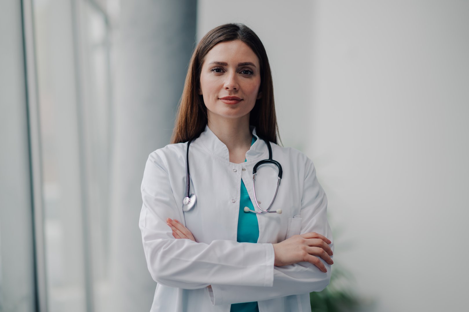 Portrait of a confident young female doctor with stethoscope, posing with crossed arms in a modern hospital setting