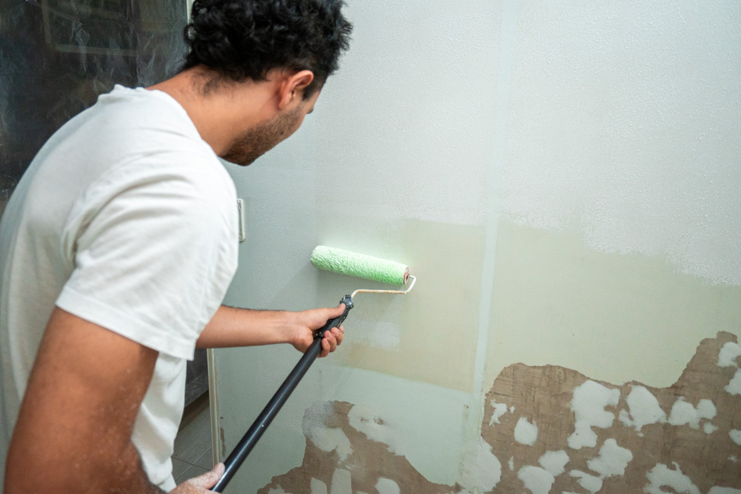 Man Painting wall with paint roller and white paint at home, copy space