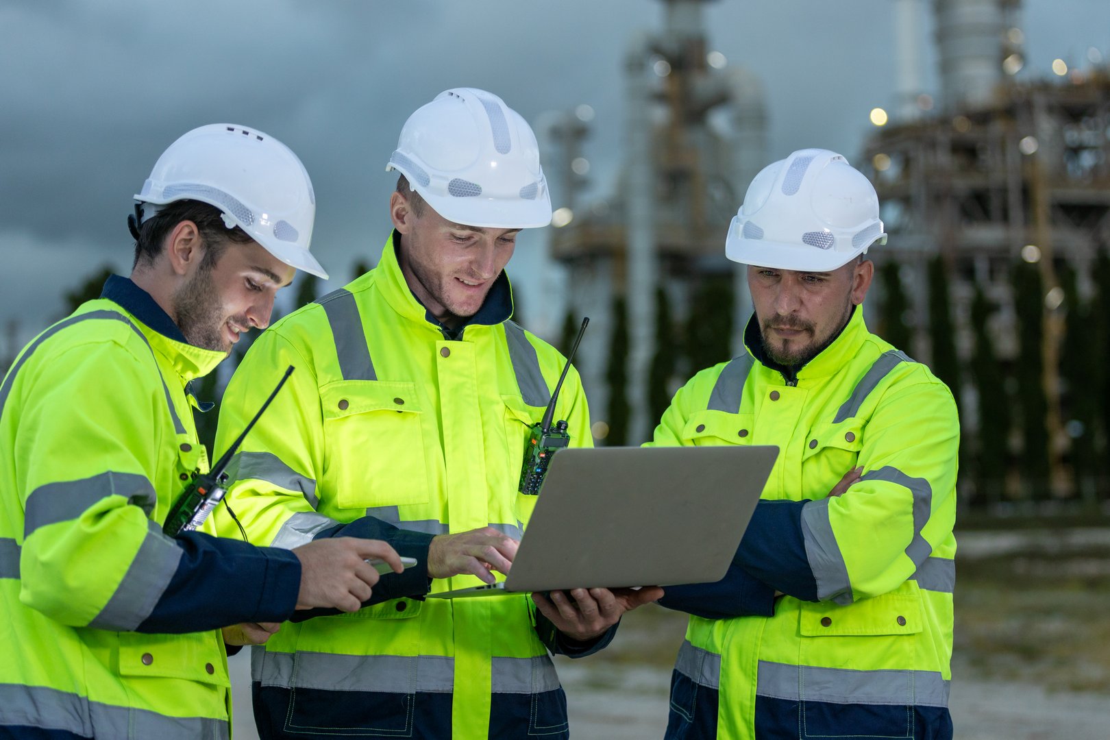 Team professional electrical engineer safety uniform working together power plant or station refining oil petrochemical using laptop evening. Industrial factory site control energy power station.