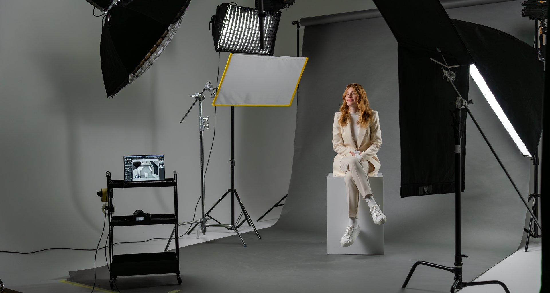Young blonde woman model at photo studio with professional equipment. Production set behind the scenes concept