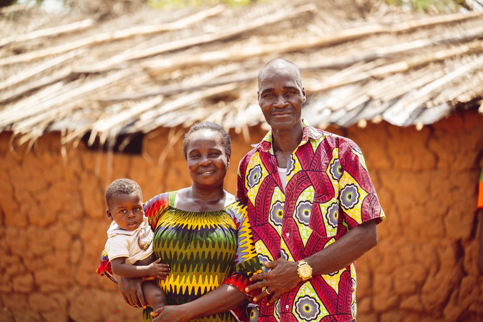 Abidjan, Ivory Coast – November 05, 2024: A family of three posing in front of a traditional clay house with a thatched roof