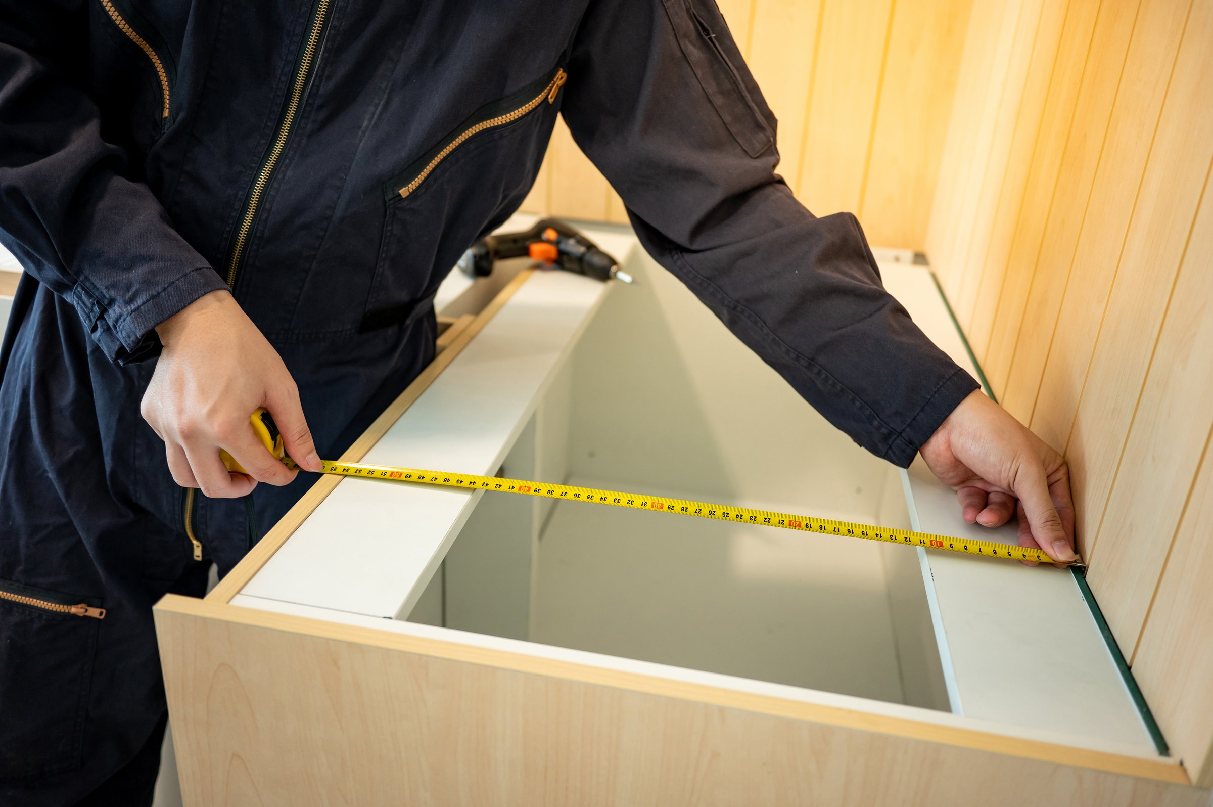 Home renovation or House remodeling concept. Male hand furniture assembler or Interior construction worker man using tape measure installing wooden counter and cabinet of the new kitchen.