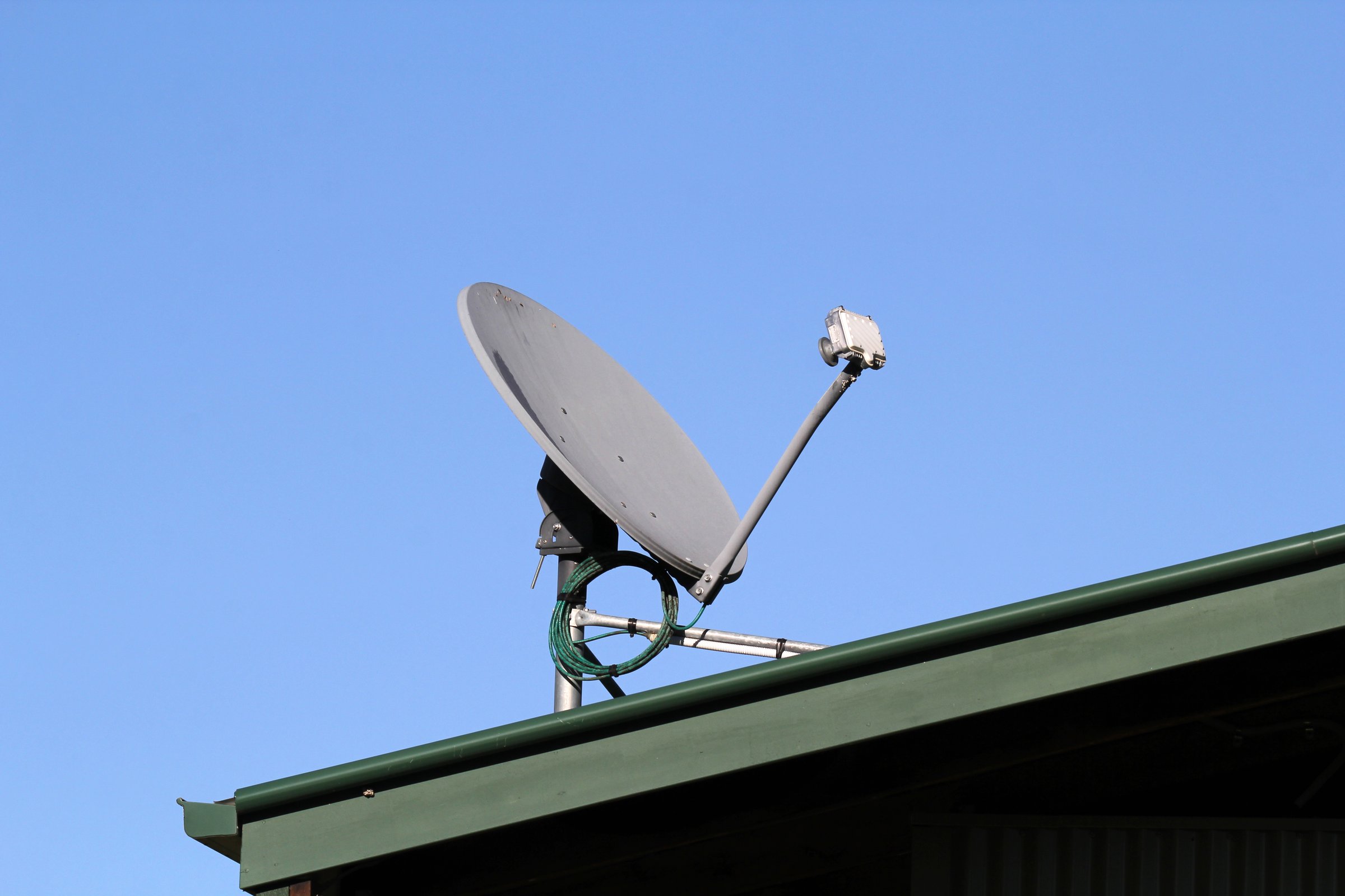 Satellite dish mounted on a green roof against a clear blue sky