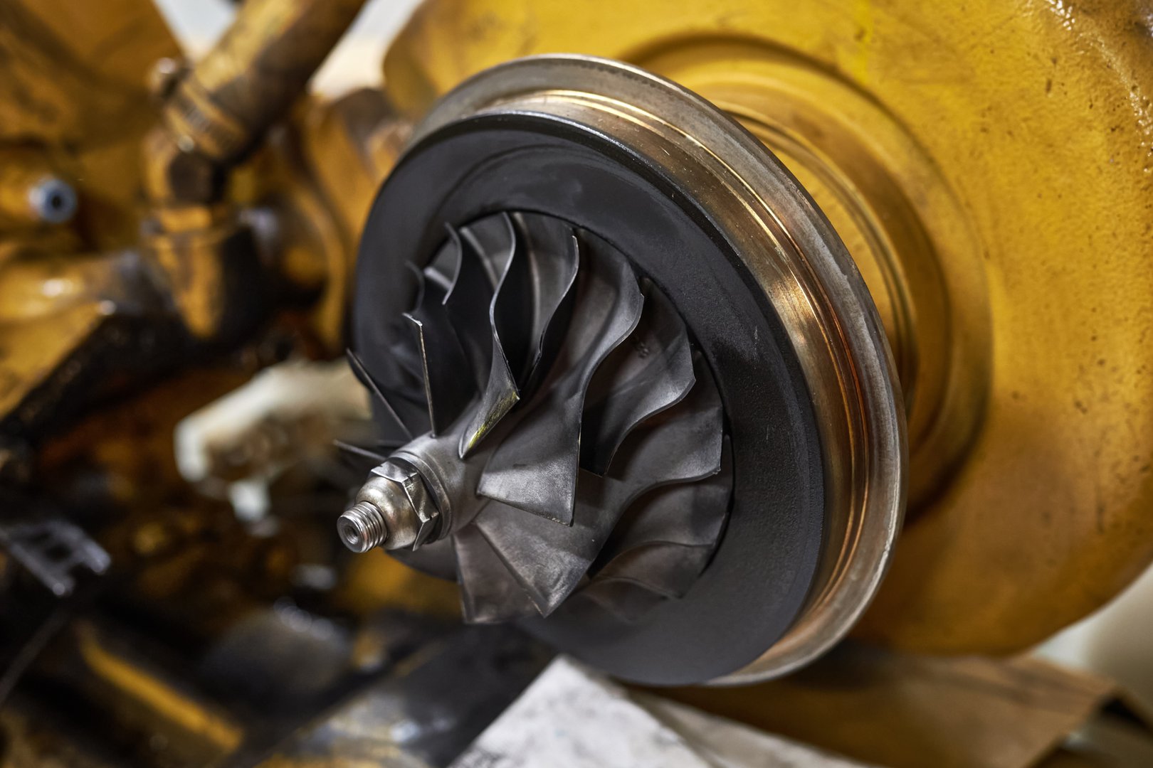 Close up of a compressor side of turbocharger assembly with blades covered in carbon soot deposits.