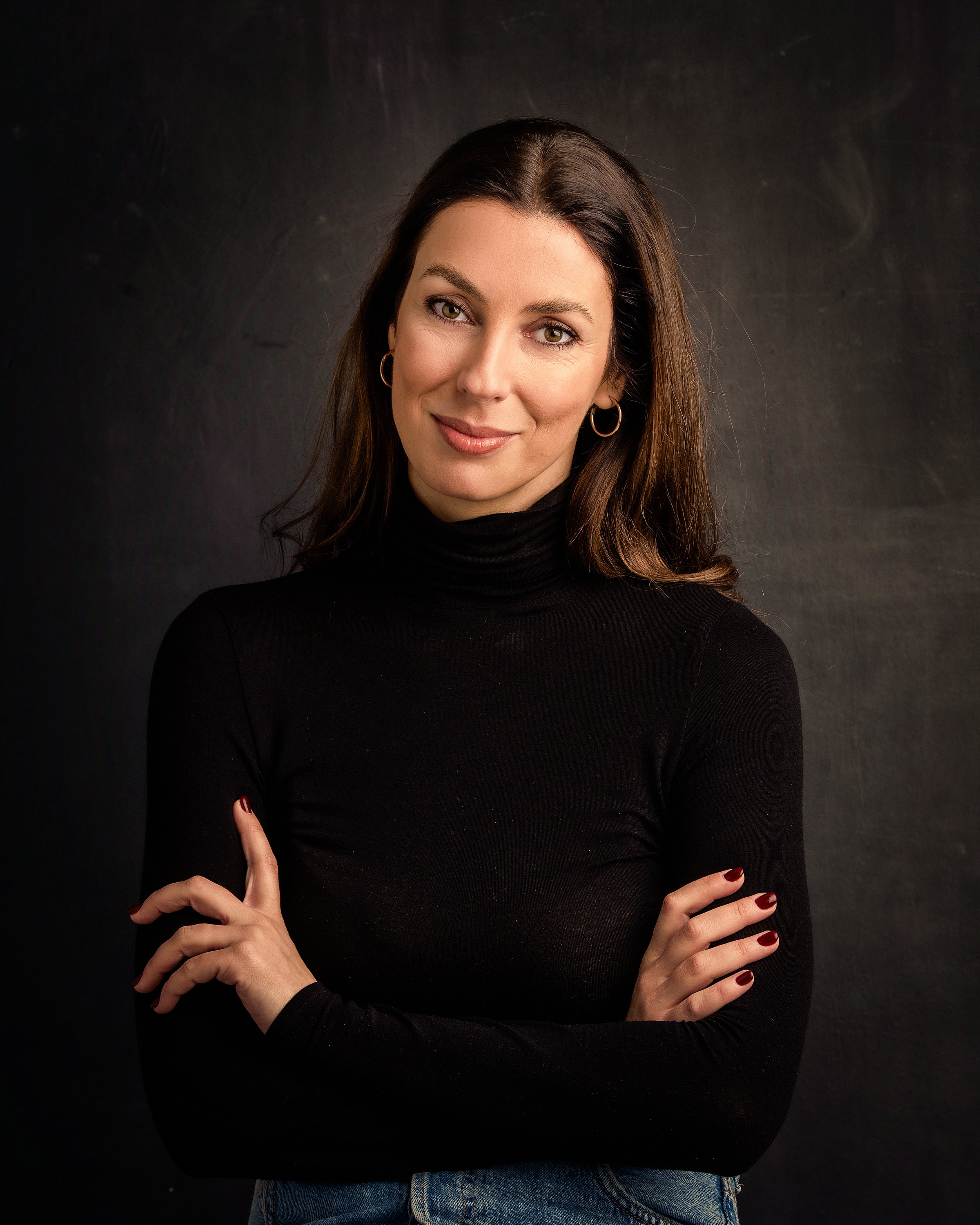 Brunette haired woman smiling against dark bacground. Attractive female wearing turtleneck sweater. Copy space.