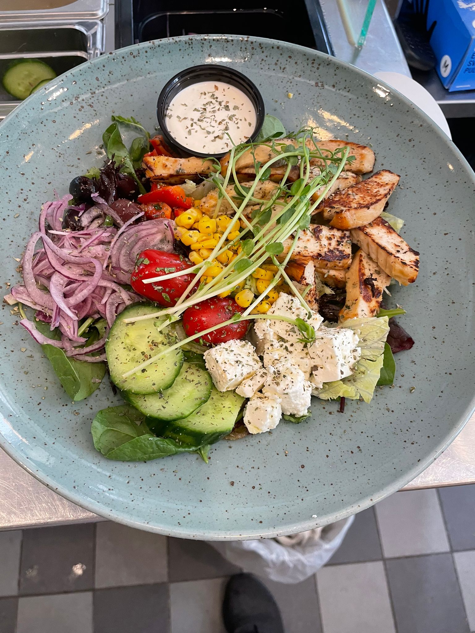 A colorful salad with grilled chicken, cucumber, feta, cherry tomatoes, corn, red onion, and dressing on a green plate.