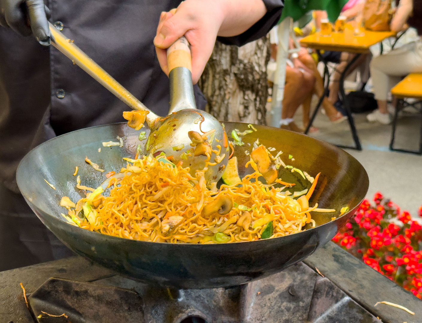 Chef stir-frying asian noodles in outdoor market scene, lifestyle