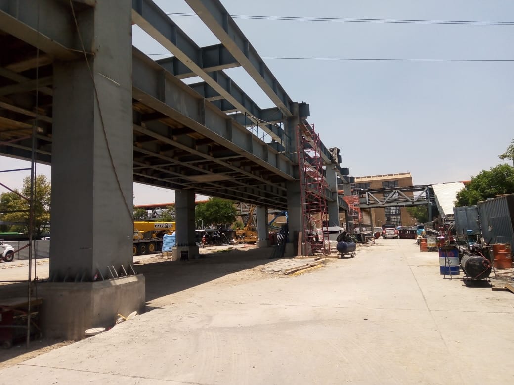 Construction site with a large metal structure, scaffolding, and equipment. Clear sky in the background.