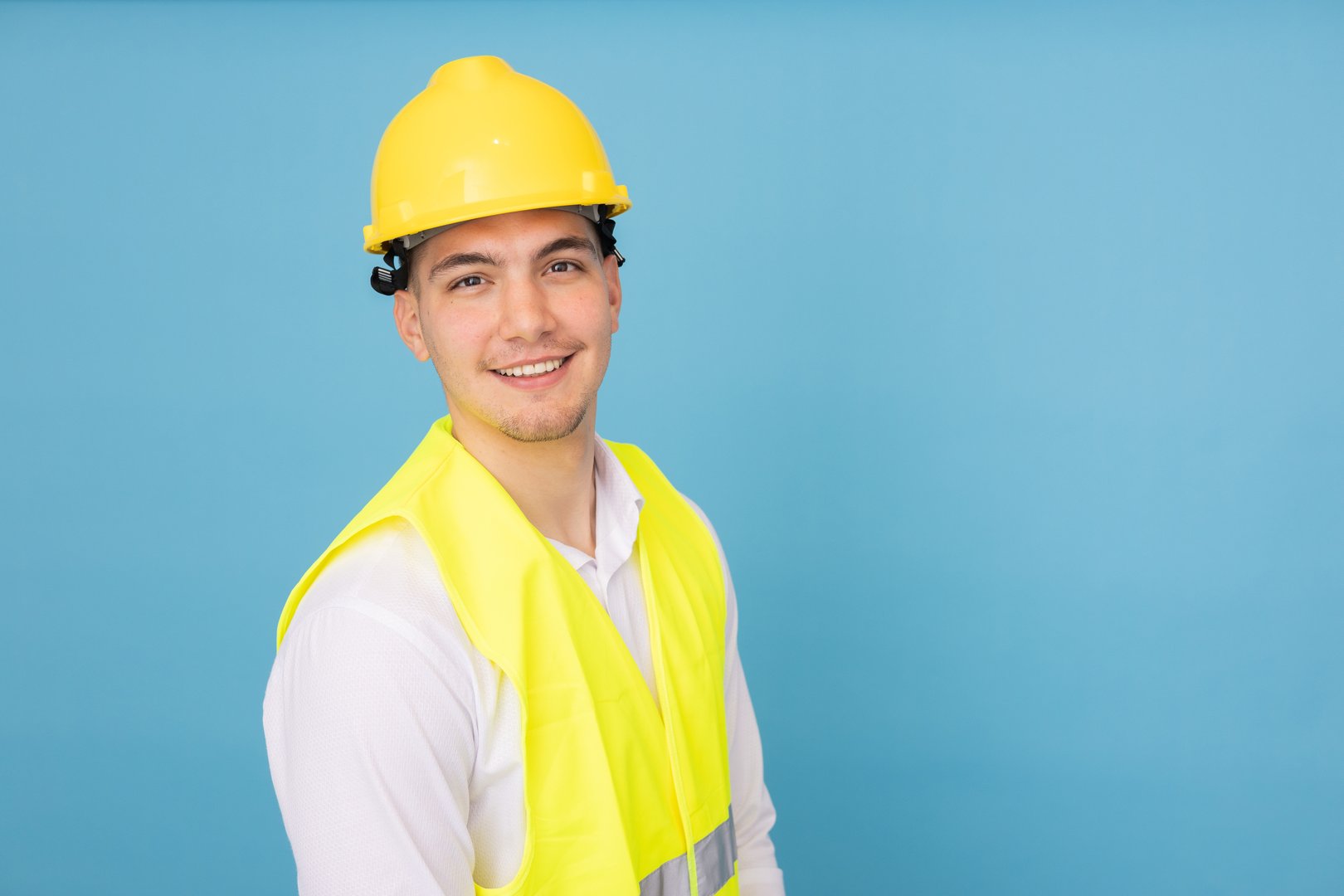 Young construction engineer smiling confidently during studio photoshoot, standing against vibrant blue backdrop