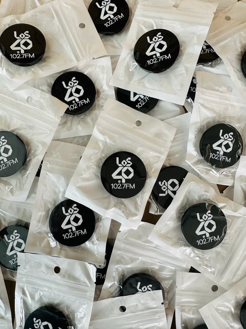 Black "Los 40 102.7 FM" phone grips in clear packaging, scattered randomly on a surface.