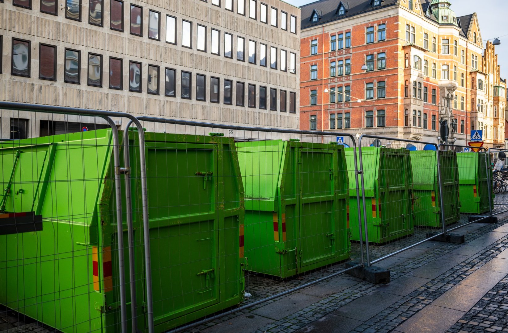 Green construction waste containers behind fence on urban street