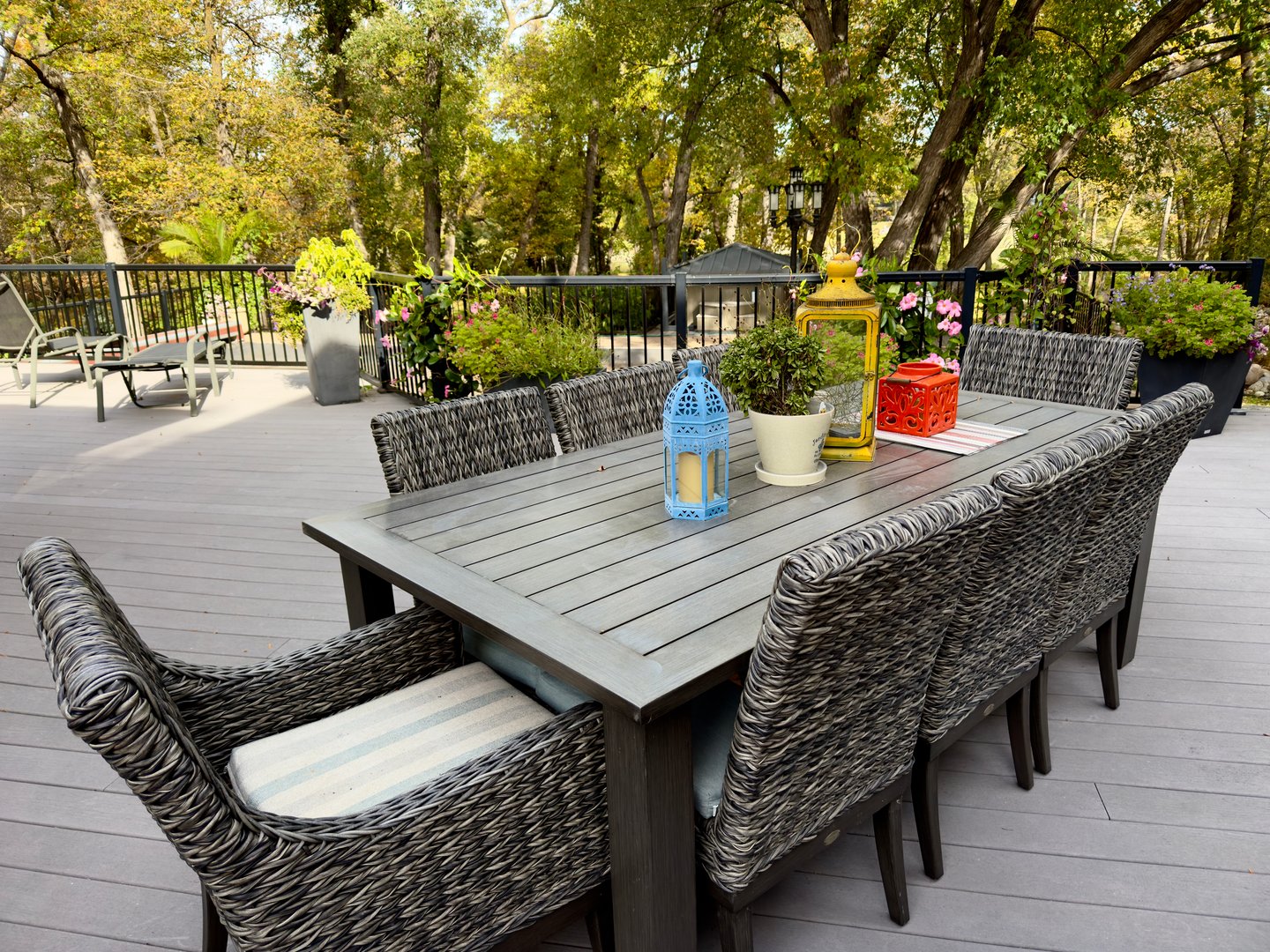 outdoor wooden table with woven chairs, decorated with lanterns and plants, terrace with garden view