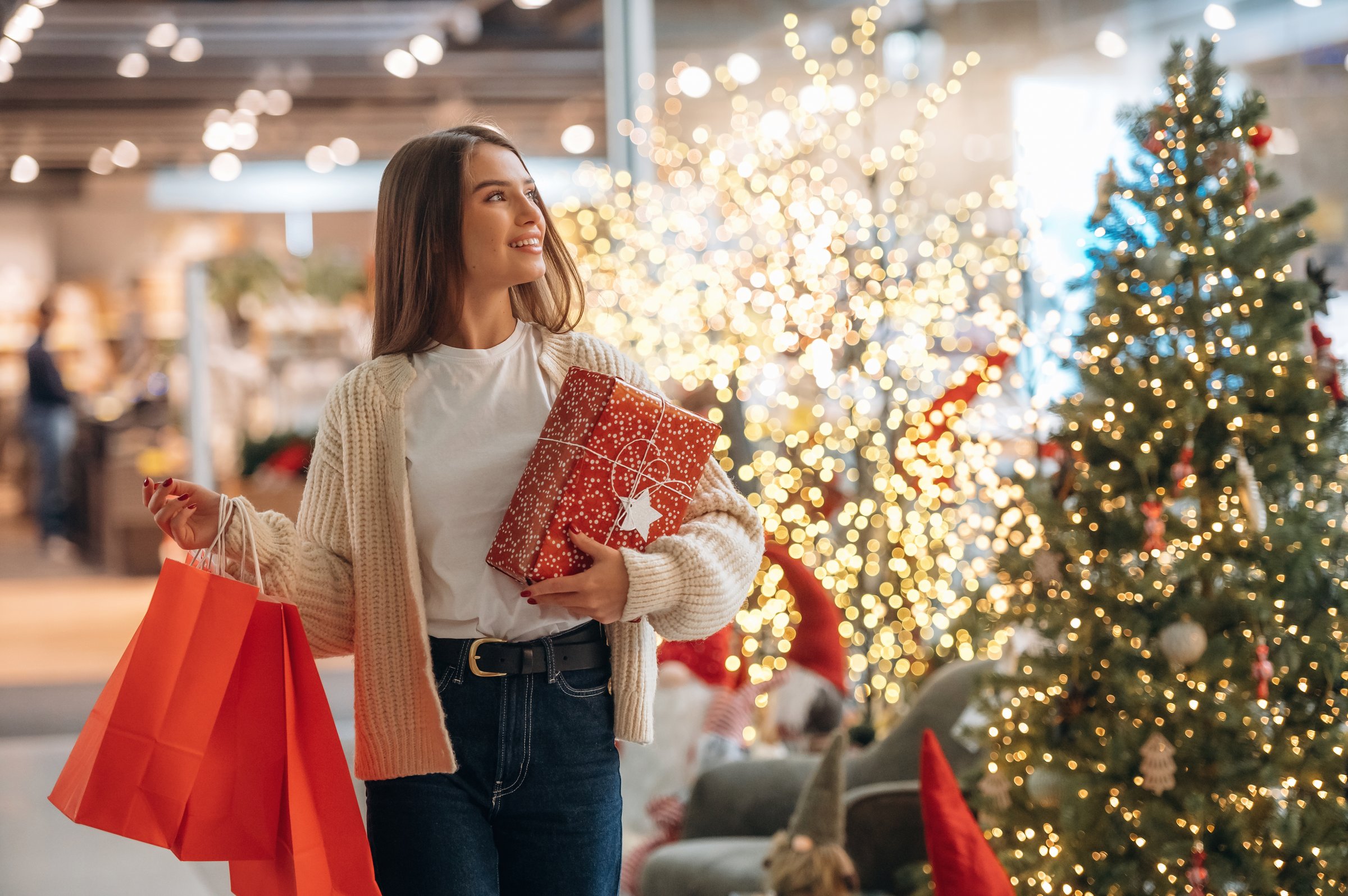 Garlands behind. New year shopping and presents. Woman is near the Christmas tree.