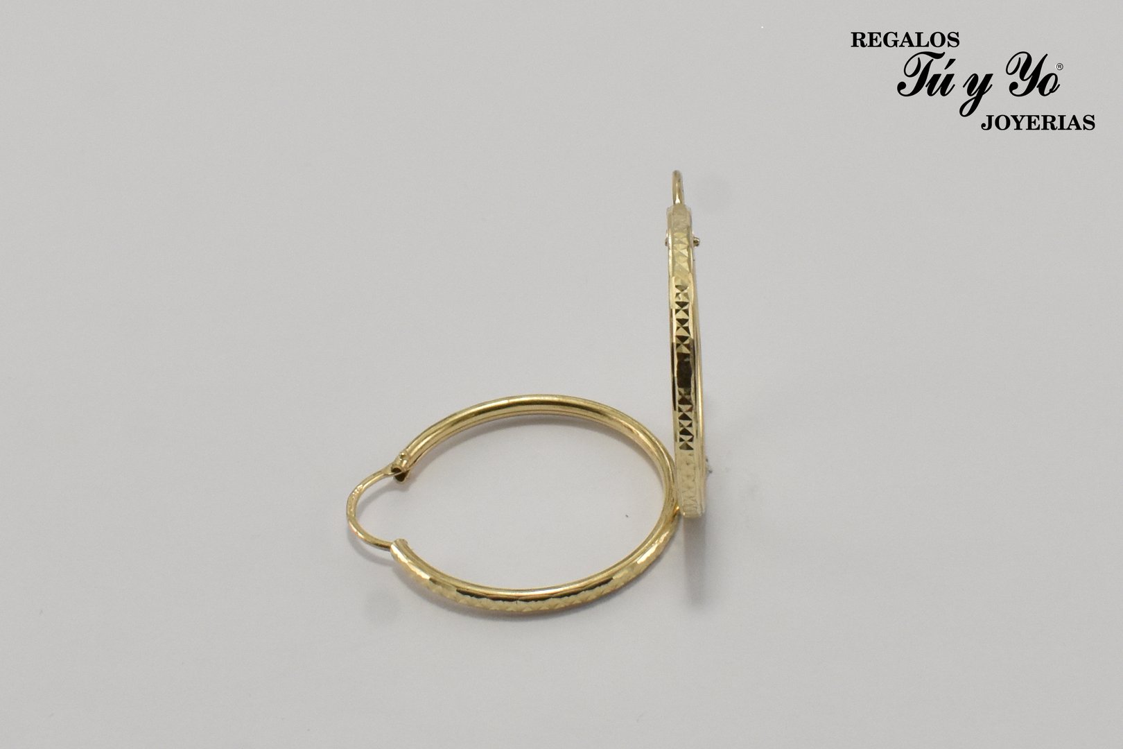 Gold hoop earrings with engraved design on a plain background, labeled 'REGALOS Tú y Yo JOYERIAS' in the corner.
