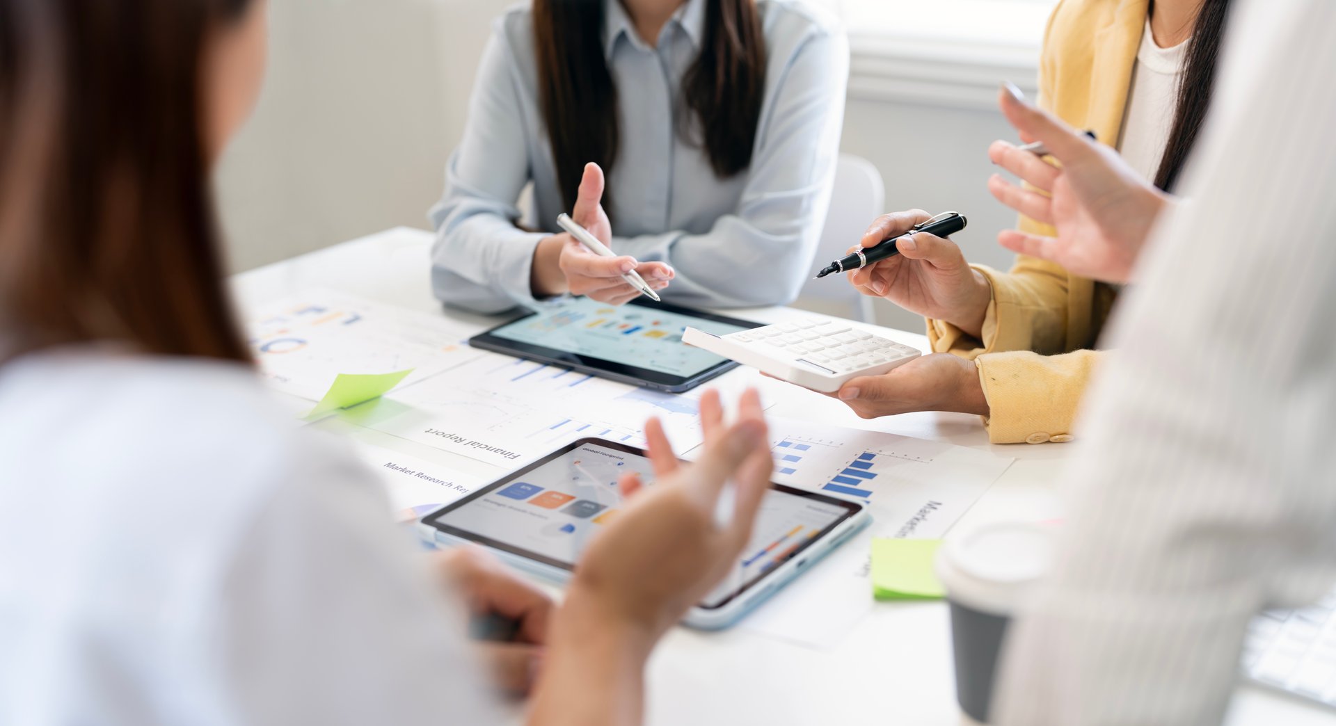 Close-up of business people discussing financial data and charts during a team meeting with tablets and calculator in modern office.