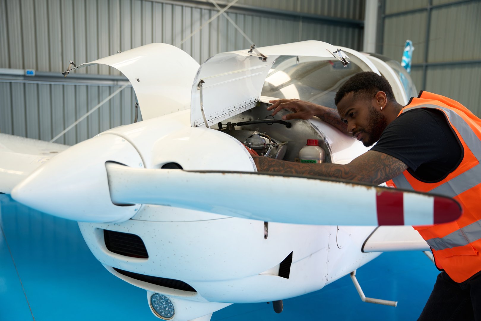 Young man working diligently as an aircraft mechanic, inspecting the engine of a small airplane inside a spacious hangar