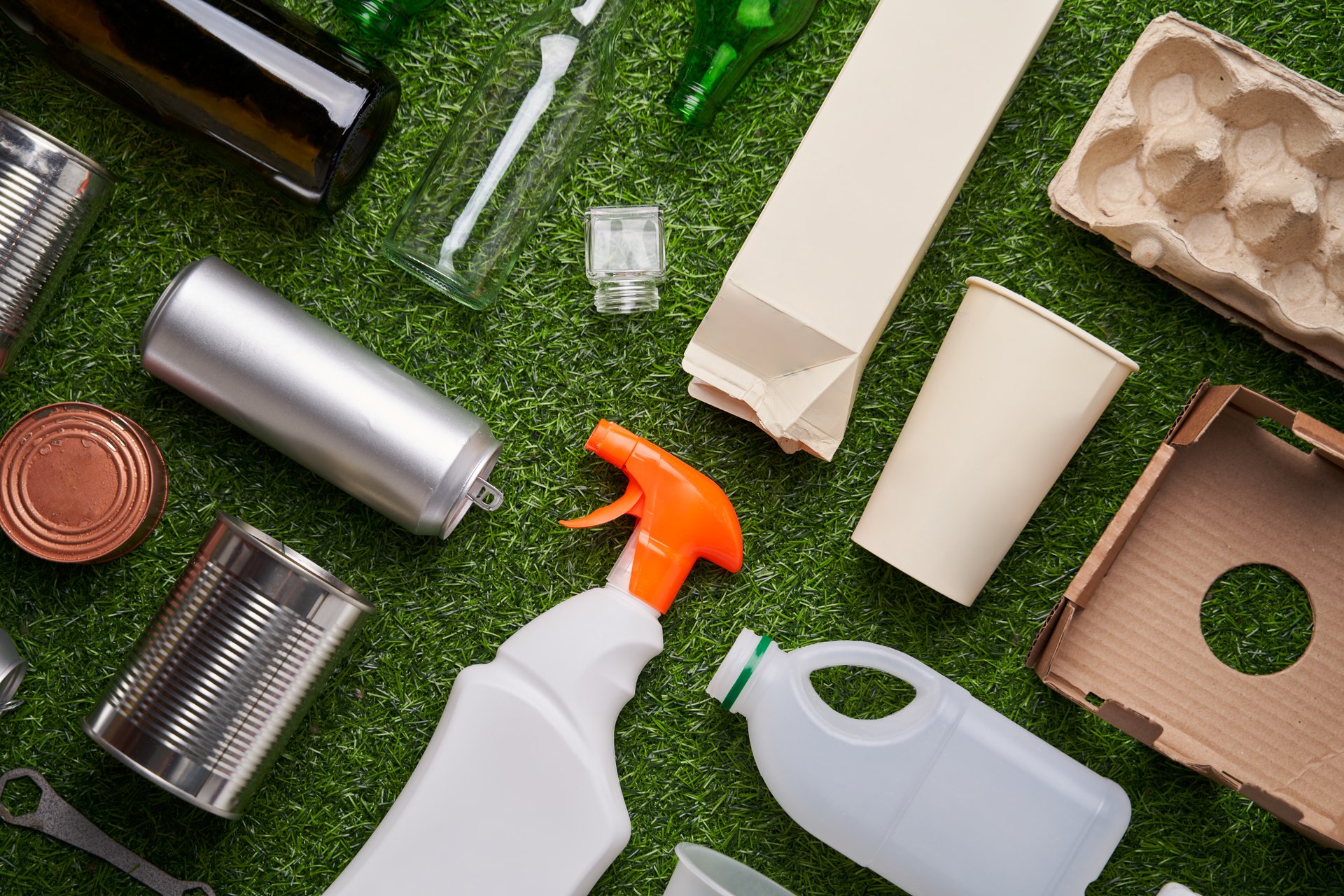 A selection of garbage for recycling. Segregated glass, metal, plastic and paper on green grass background. Concept of zero waste, eco lifestyle and sustainable living