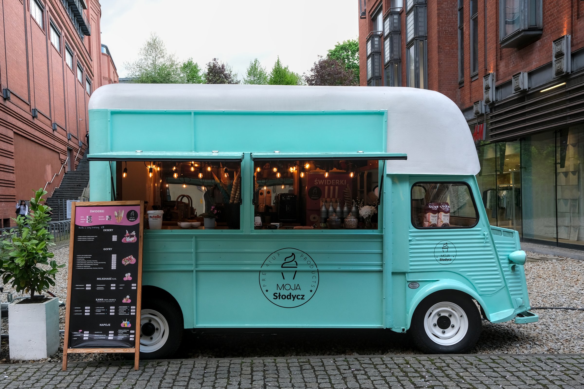 Poznan, Poland - 04 22 2025 : A turquoise food truck named "Moja Słodycz", My Sweetness in poish, is parked in an urban area, offering desserts and beverages, with a menu board and decorative lights.