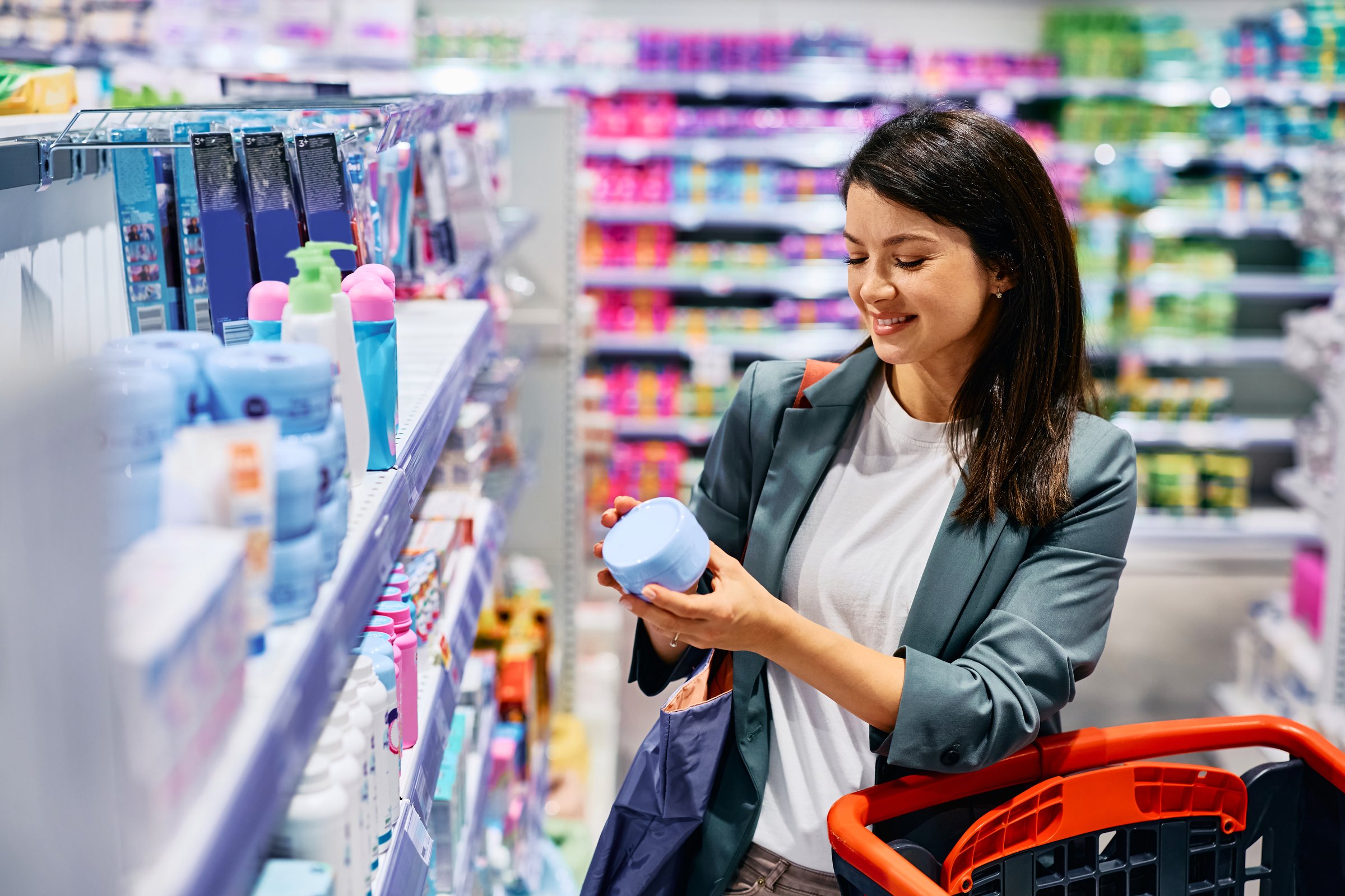 Happy woman choosing moisturizer while shopping at supermarket. Copy space.