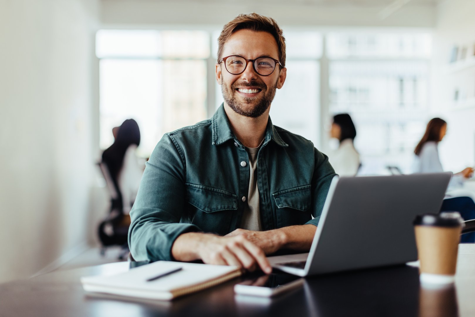 Portrait of a business man sitting in an office with his colleagues in the background.