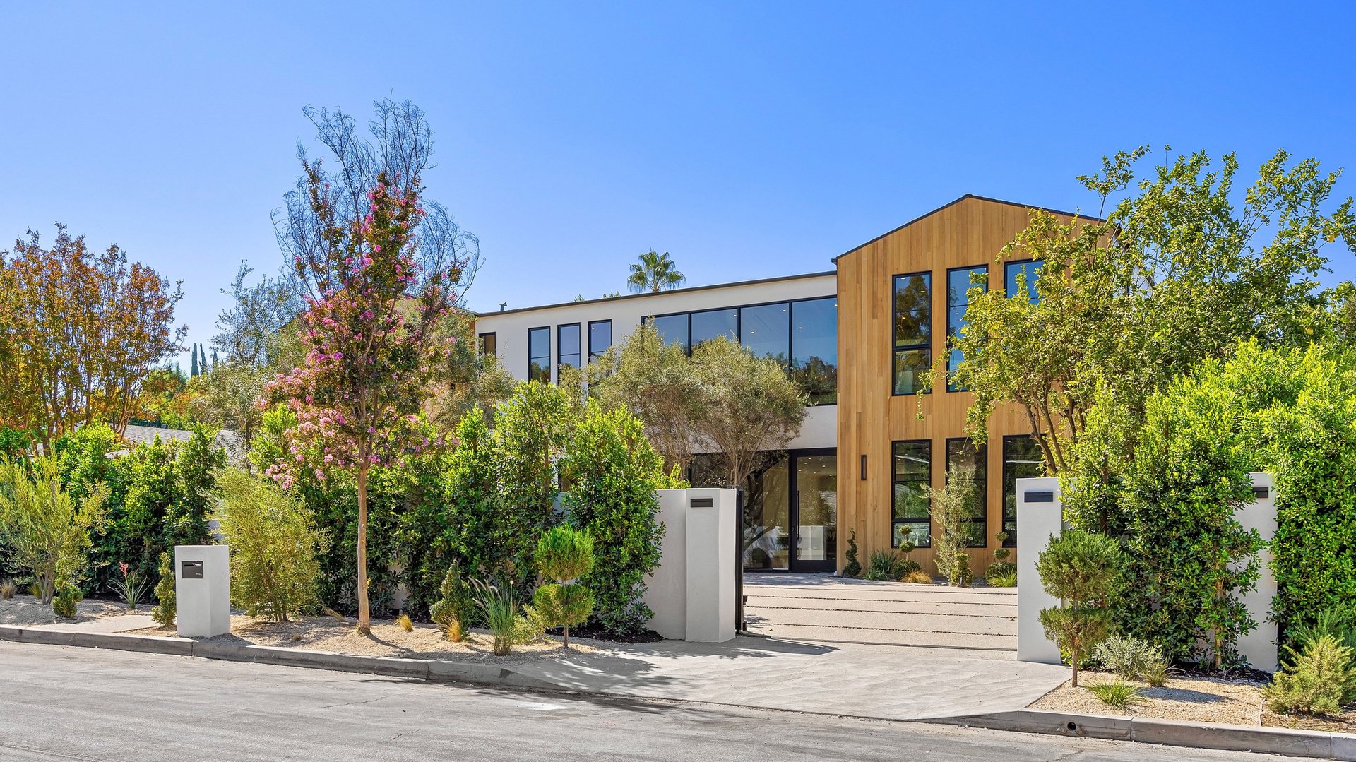 Modern luxury home exterior with wooden facade and lush landscaping under a clear blue sky.