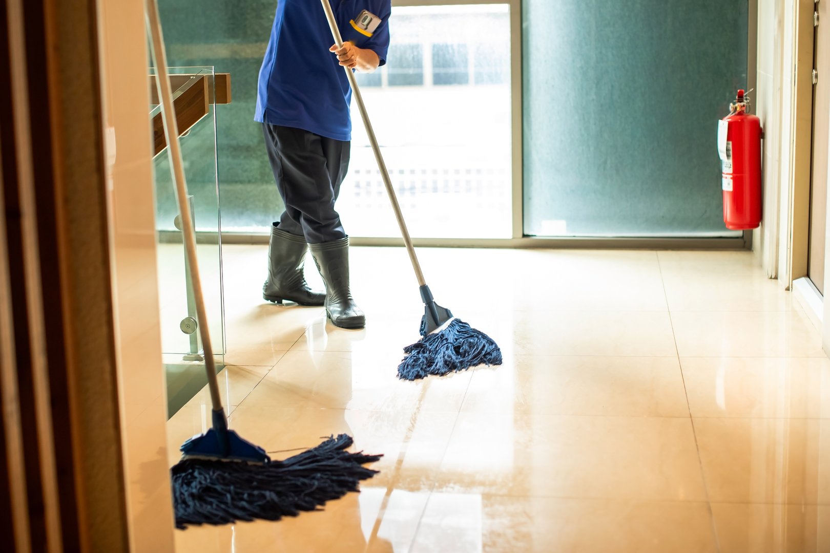 Housekeeper mopping the floor with a mop and cleaning products to clean dust in a condominium corridor. Cleaning dirty floor with mop in office building.