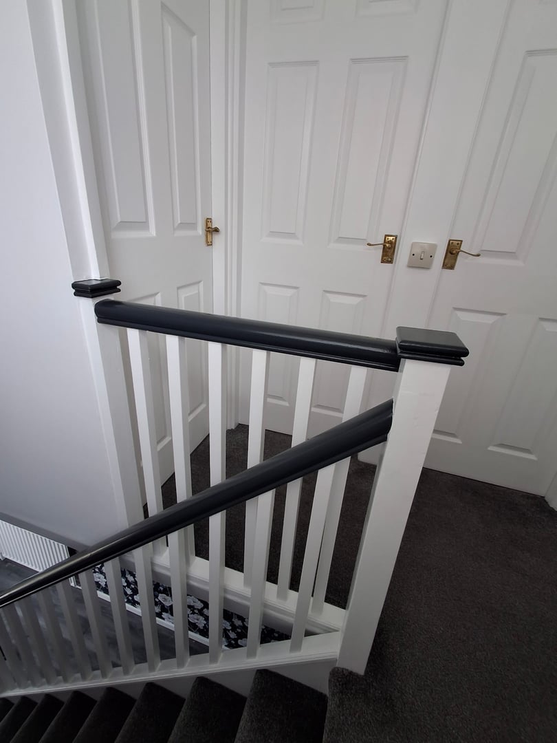 A modern staircase with dark handrails and gray carpet, leading to two closed white doors with golden handles.