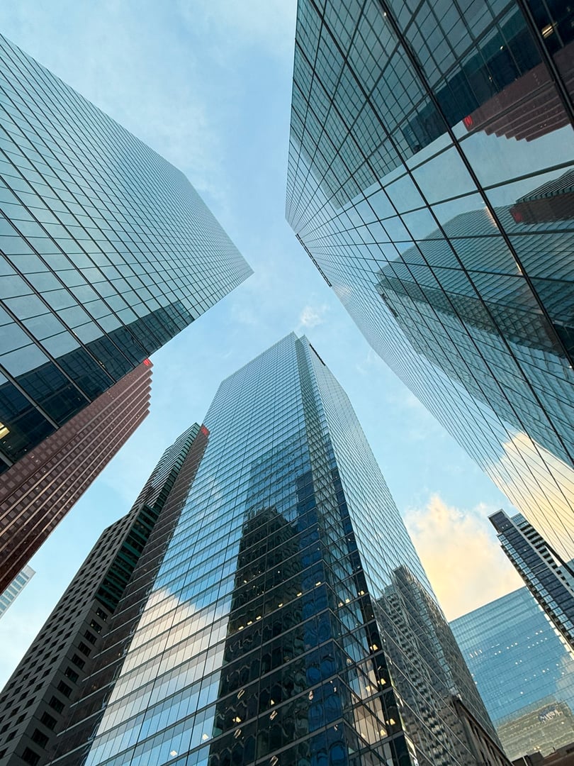 Low angle view of modern glass skyscrapers reflecting the sky and surrounding city buildings. Contemporary urban skyline in a business district, symbolizing architecture, corporate growth, finance, and real estate development