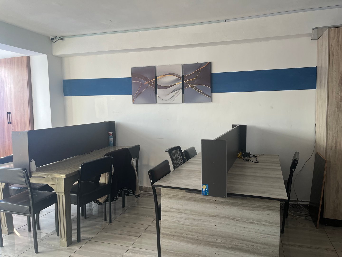 A modern office space with desks, chairs, wall art, and a striped wall decoration in blue and gray tones.