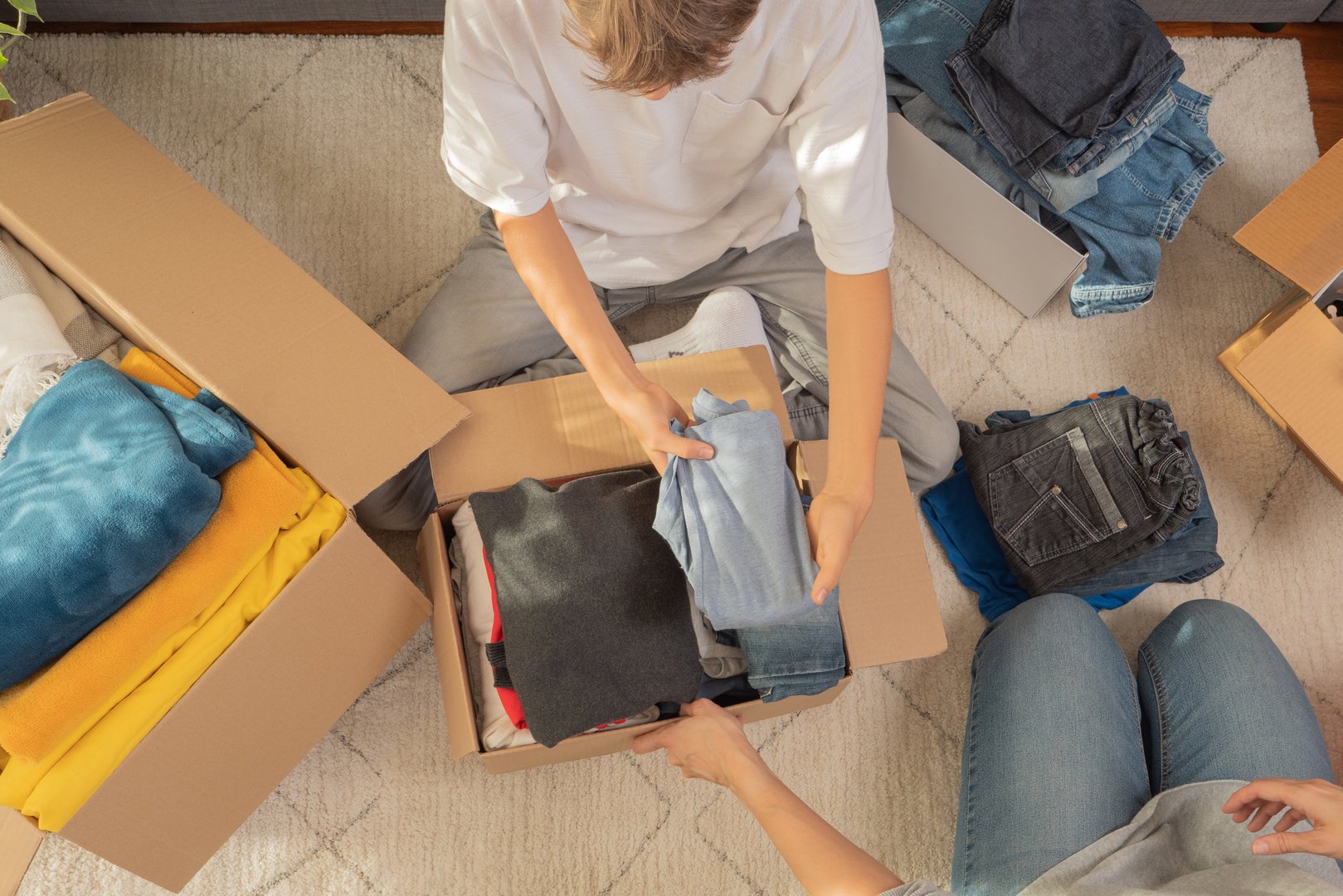 Woman and child sorting clothes and packing into cardboard box. Donations for charity, help low income families, declutter home, sell online, moving moving into new home, recycling, sustainable living.