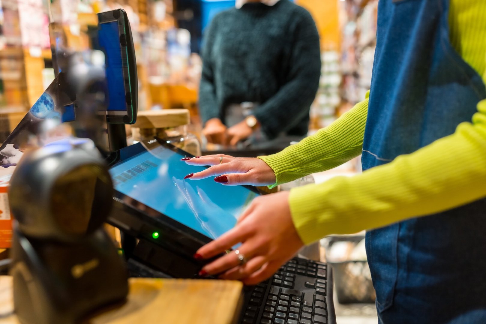 Saleswoman processing a customer's purchase at the point of sale system in an organic supermarket, using a modern touchscreen cash register