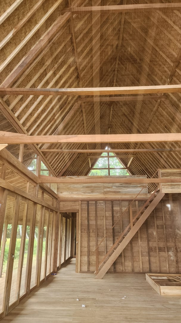 Interior view of a wooden house under construction, featuring an exposed wooden framework and a loft with angled ceiling.