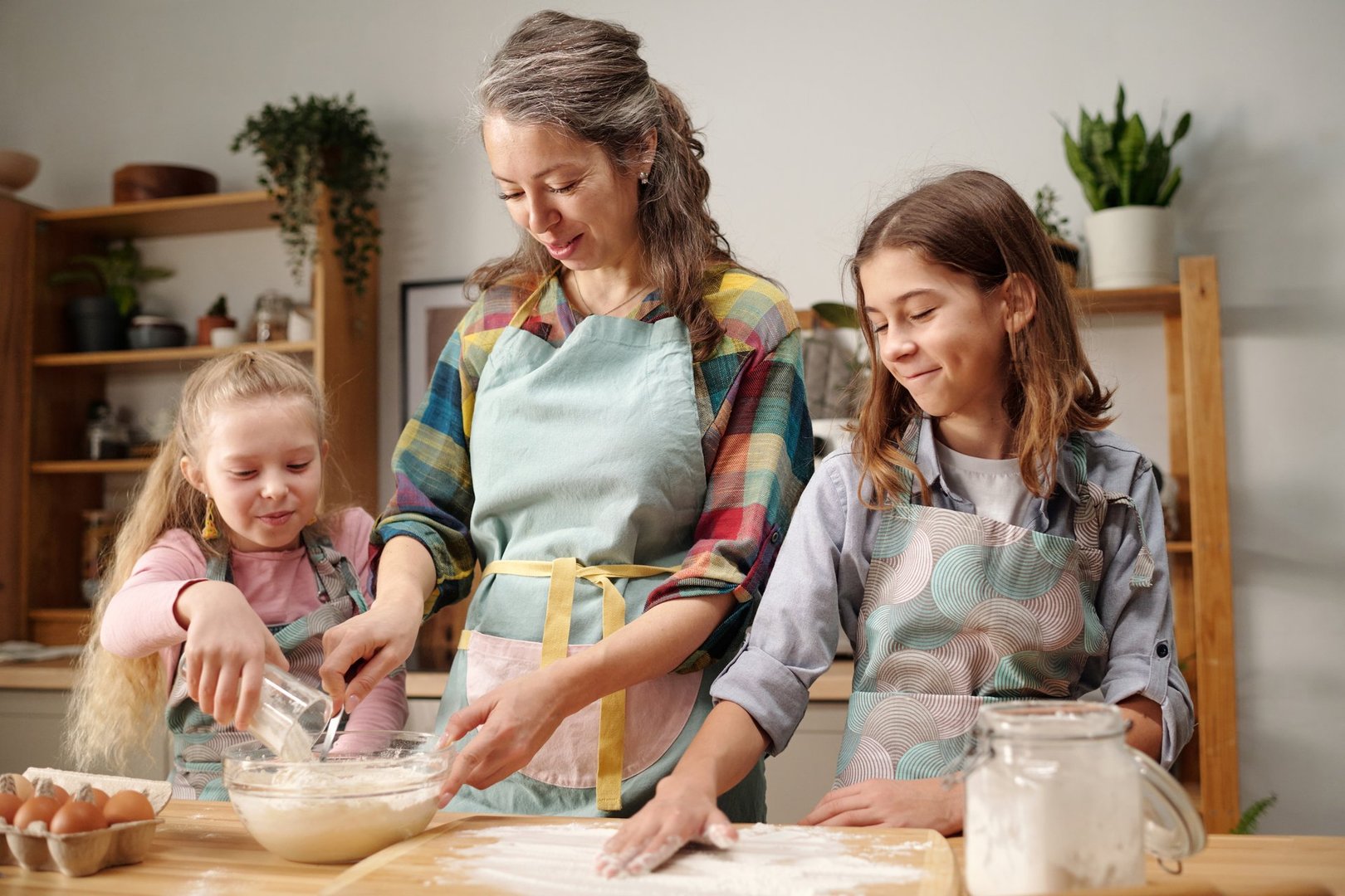Mother baking with her daughters in cozy kitchen setting, mixing ingredients and enjoying time together while preparing dough and batter