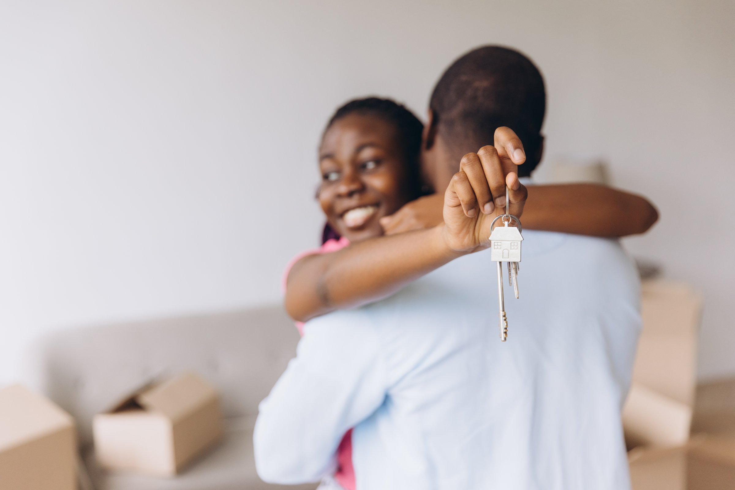 Excited African American couple embracing each other while proudly displaying keys to their new home, celebrating a significant milestone in homeownership